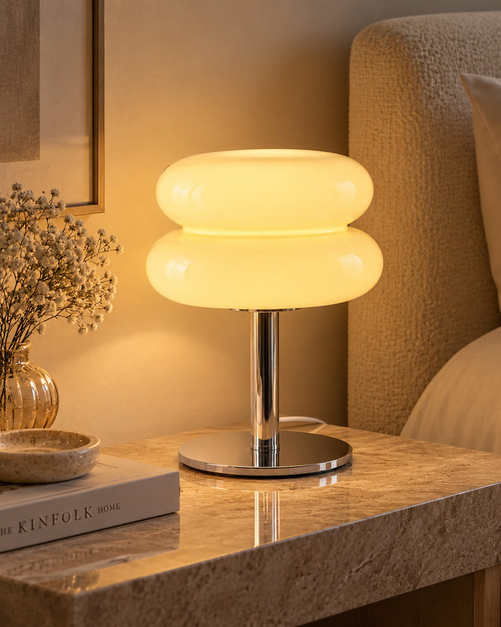 Cream two-tier glass macaron lamp glowing warm white on a marble side table beside a sofa