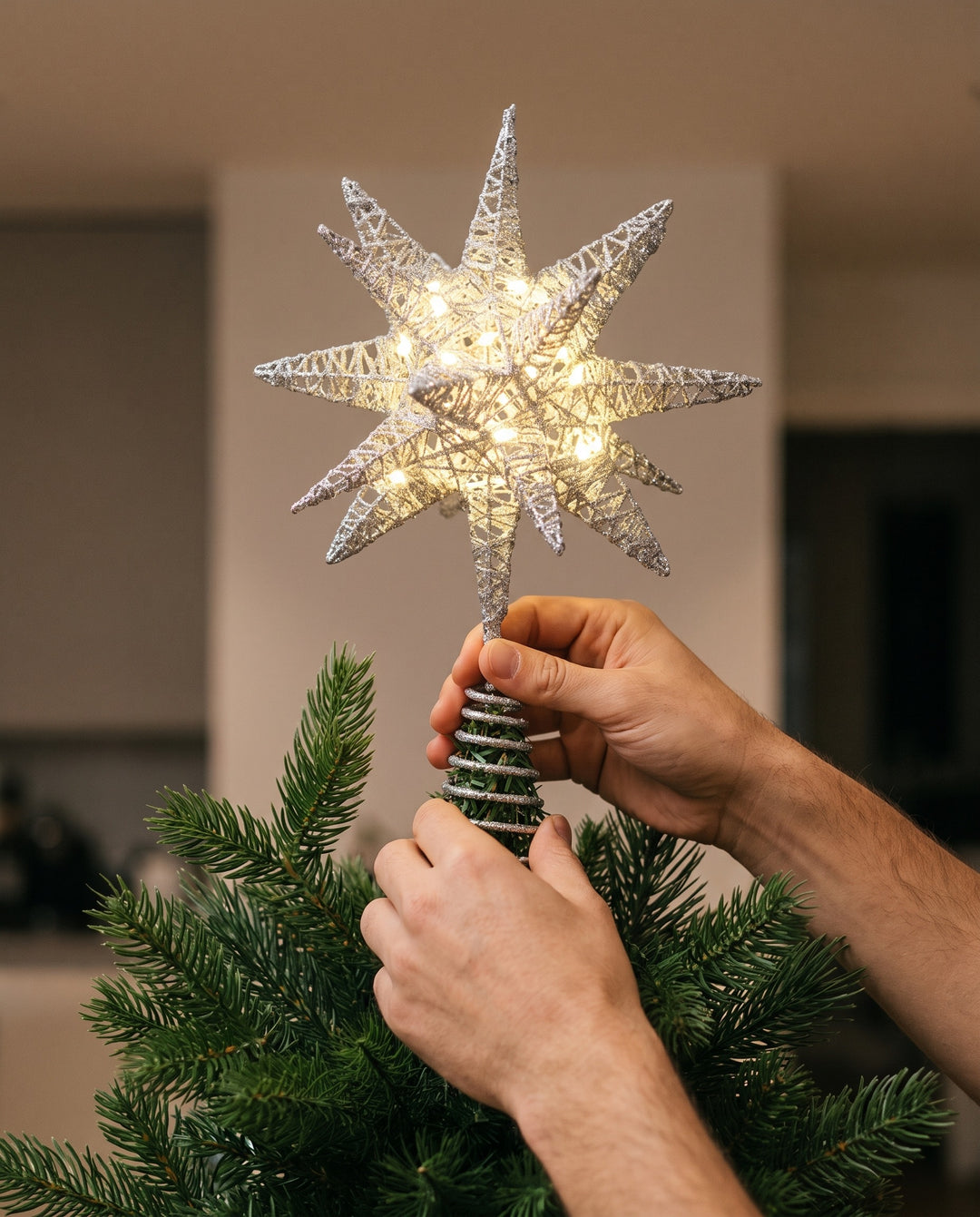 Hands sliding the spiral of the silver 3D star topper onto the top of a fir tree