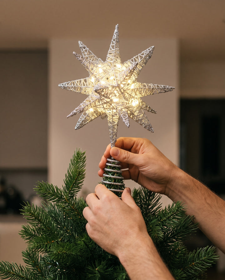 Hands sliding the spiral of the silver 3D star topper onto the top of a fir tree
