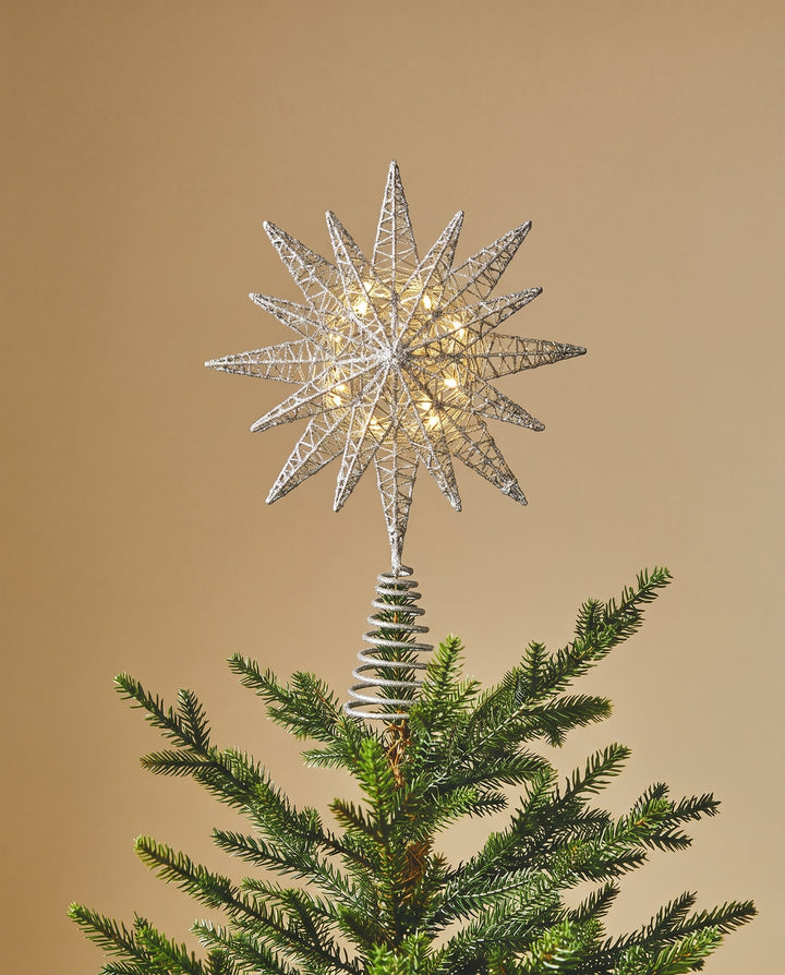 Silver 3D star topper lit on a natural fir tree against a warm beige wall