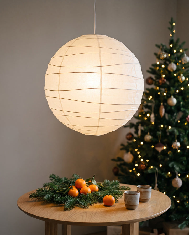 Paper lantern lit above a small round oak table with fir branches and clementines at Christmas