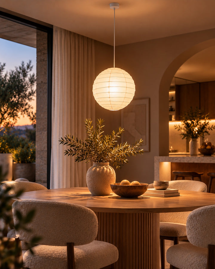 Round paper lantern hanging above a dining table with an olive branch centerpiece
