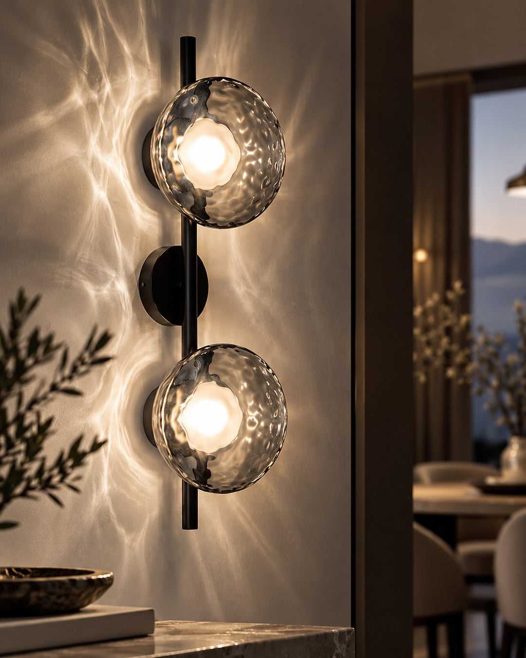 Close-up of the black double-head Orbe wall sconce with gray glass globes casting water-like reflections on the wall
