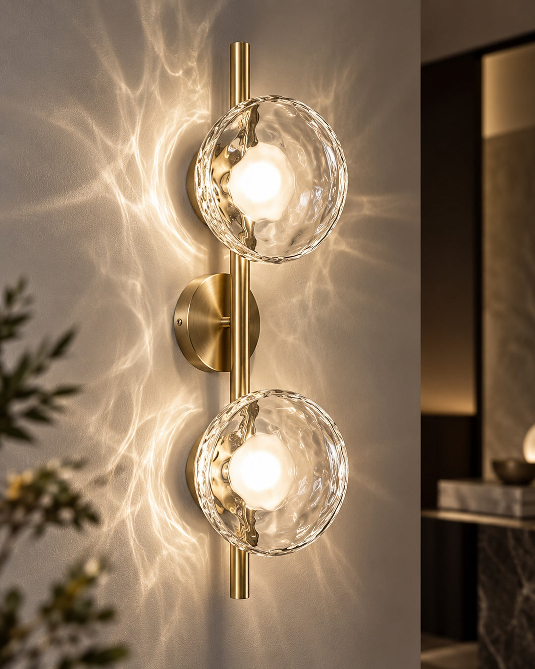 Close-up of the gold double-head Orbe wall sconce with clear glass globes casting rippled light on the wall