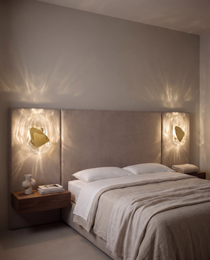 Pair of gold Ripple wall lights casting rippling light on each side of an upholstered headboard