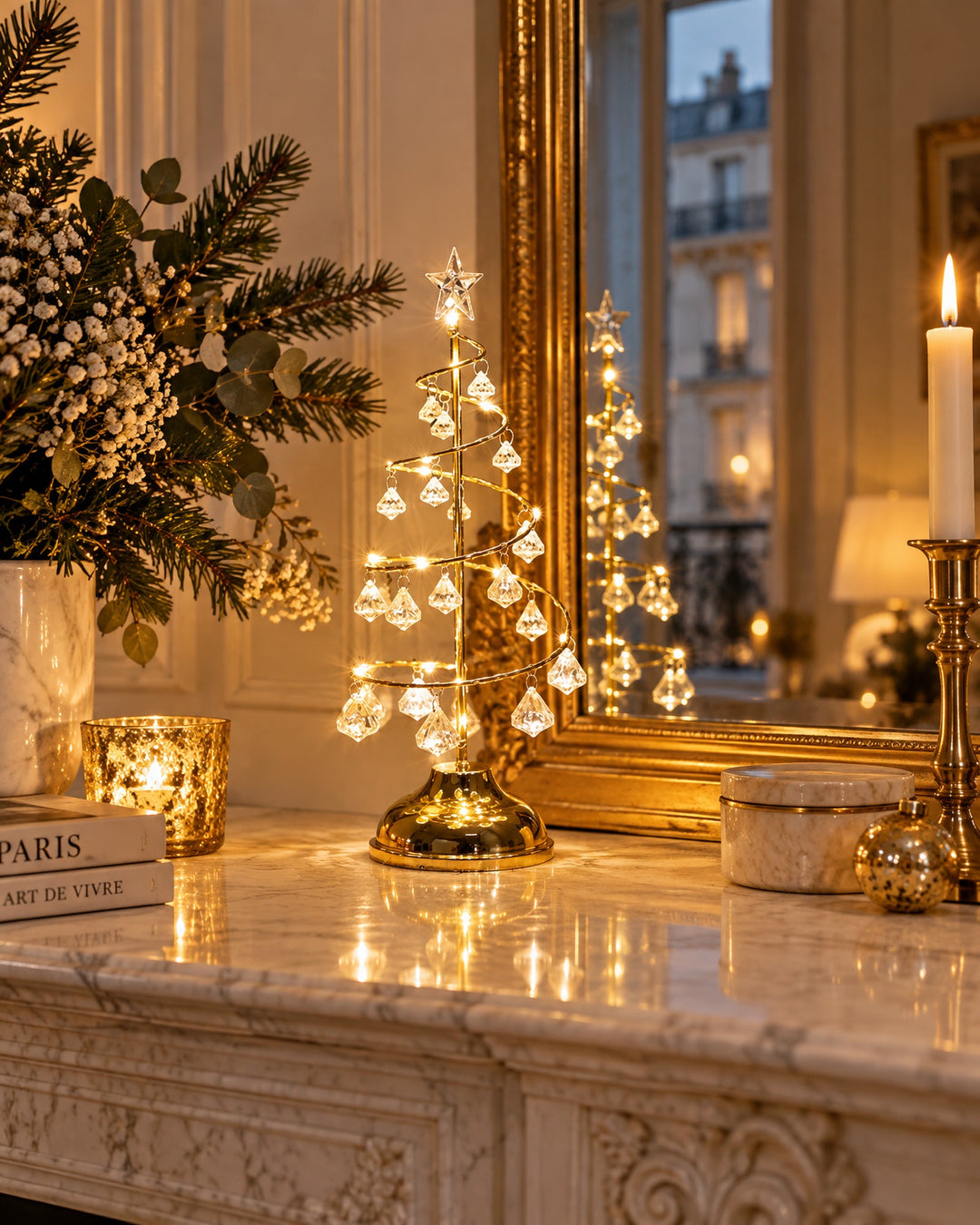 Gold-tone spiral tree light glowing on a marble mantelpiece in front of a gold mirror