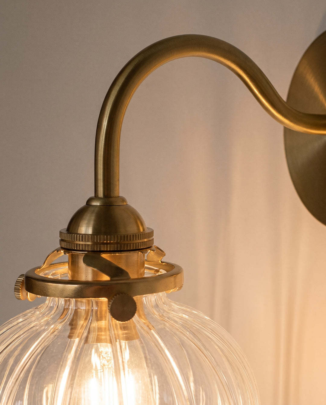 Close-up of the gold-tone copper gooseneck arm and lit ribbed glass globe