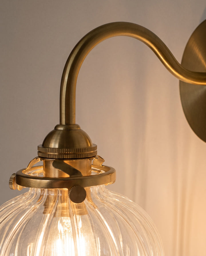 Close-up of the gold-tone copper gooseneck arm and lit ribbed glass globe