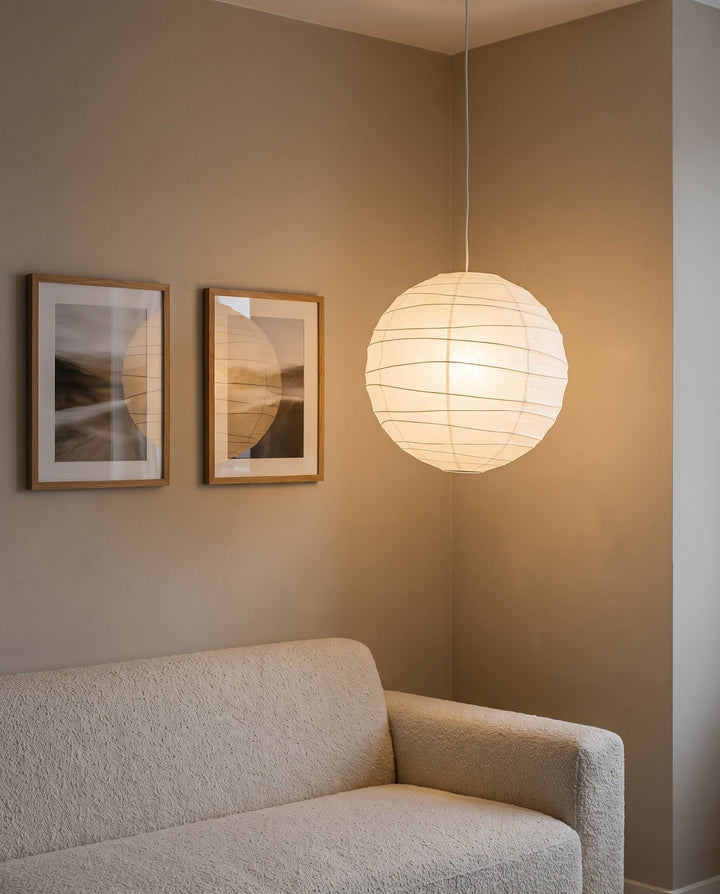Round paper lantern pendant lit above the end of a cream sofa in a living room corner