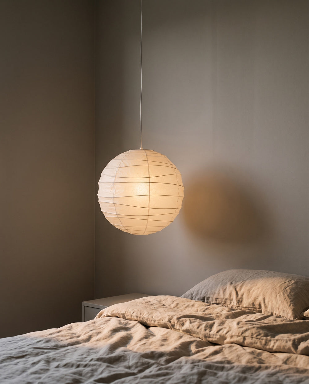 Paper lantern pendant glowing low above a bedside table at night