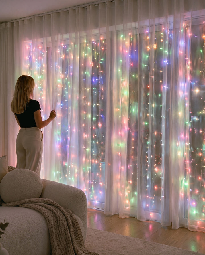 Multicolor LED fairy curtain lights glowing behind sheer curtains at a large window in a living room at night