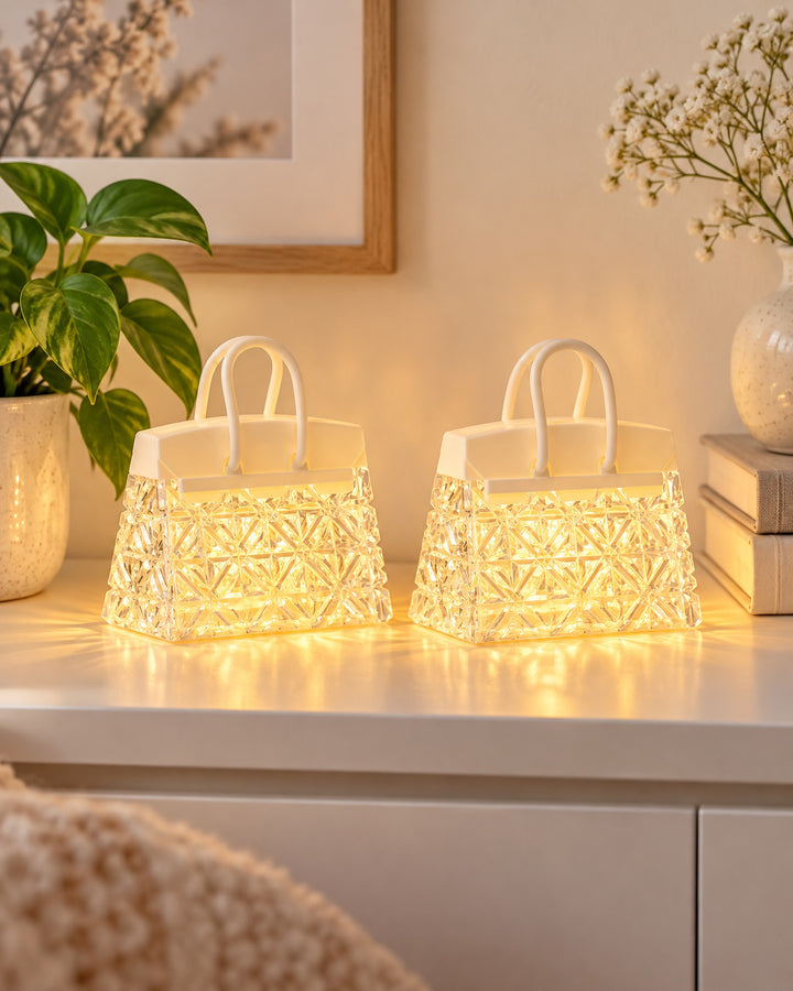 Two handbag night lights glowing warm amber side by side on a white shelf
