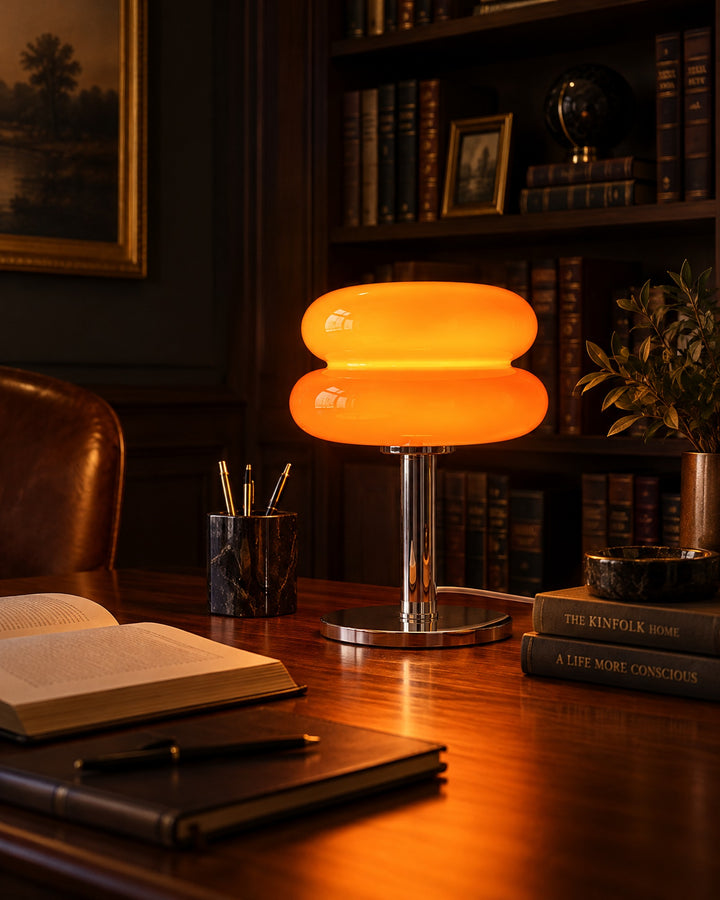 Orange two-tier glass macaron lamp glowing on a wooden desk in a dark library