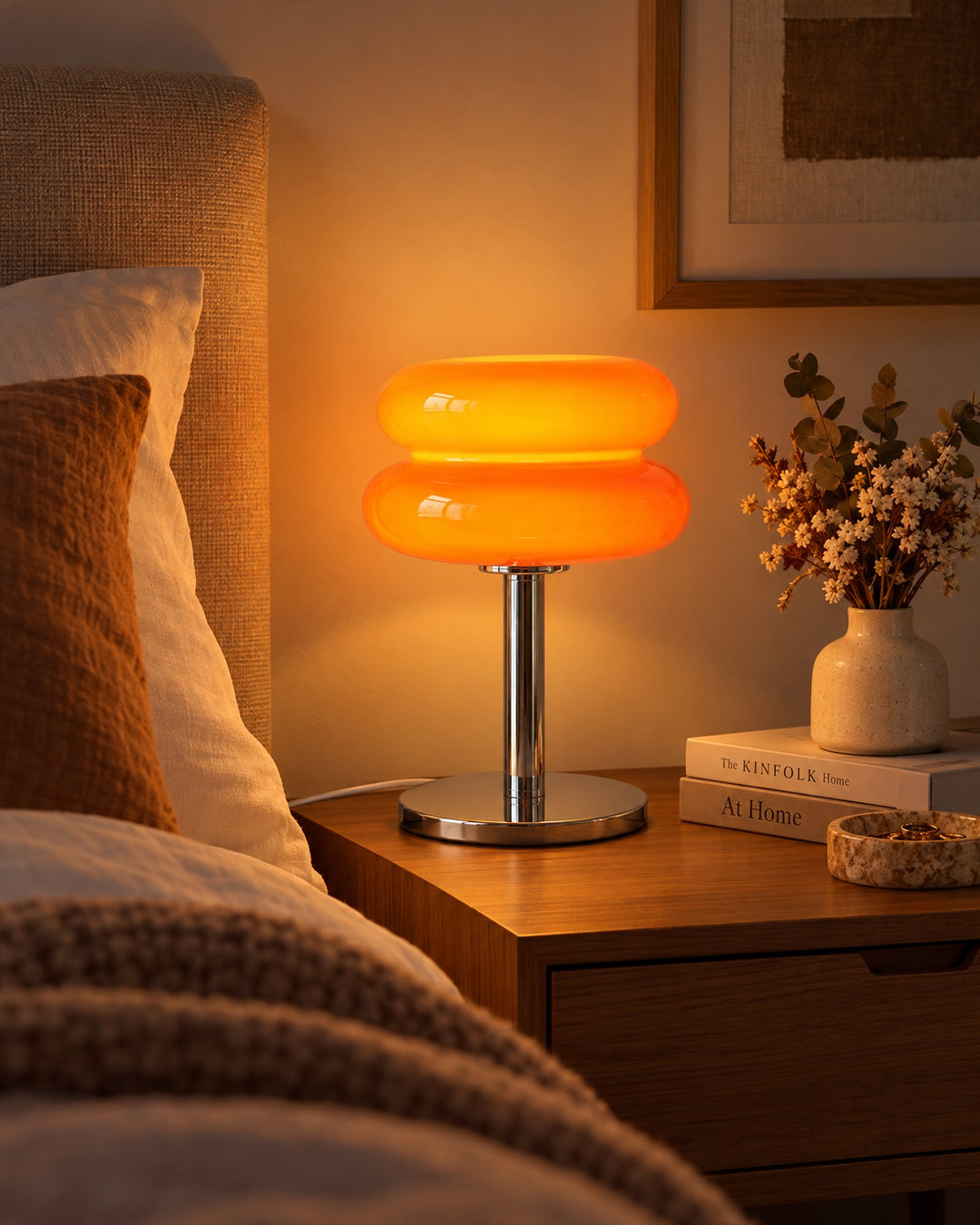 Orange macaron glass lamp glowing on a bedside table next to dried flowers