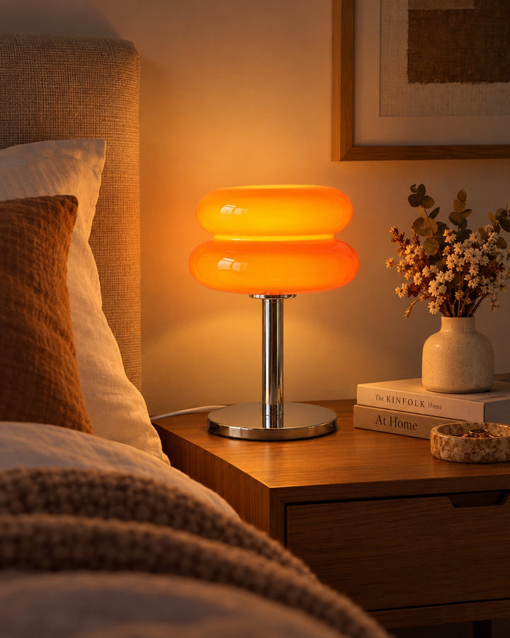 Orange macaron glass lamp glowing on a bedside table next to dried flowers