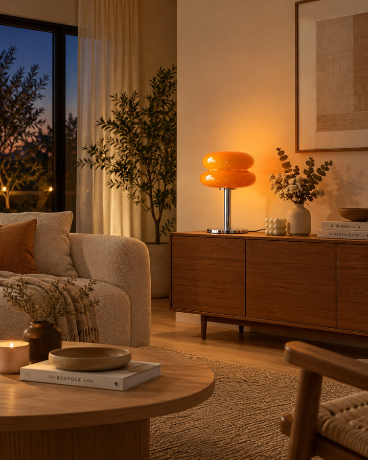 Orange macaron lamp glowing on a wooden sideboard in a living room at dusk