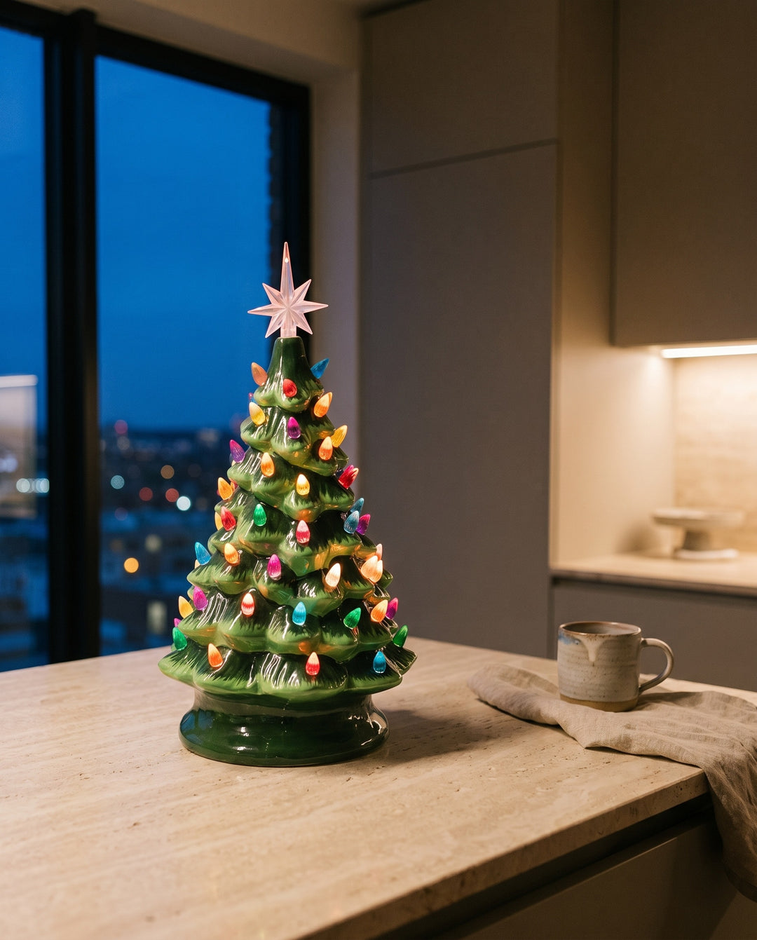 Lit vintage green ceramic Christmas tree with multicolour bulbs and a pink star on a travertine kitchen worktop at dusk