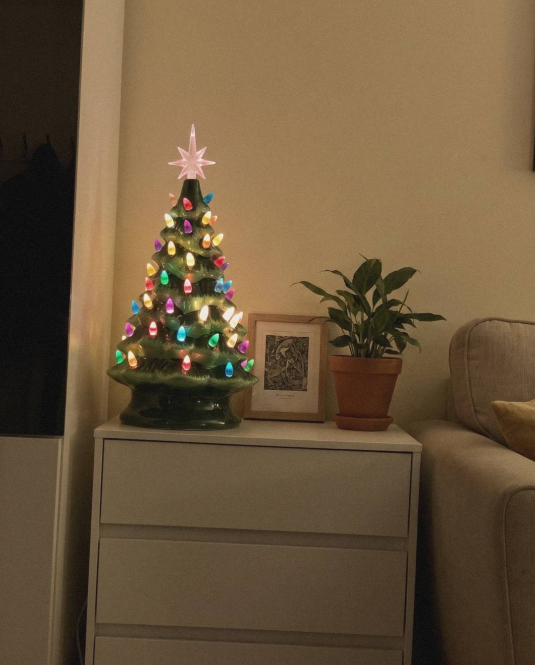 Ceramic Christmas tree glowing on a white chest of drawers at home