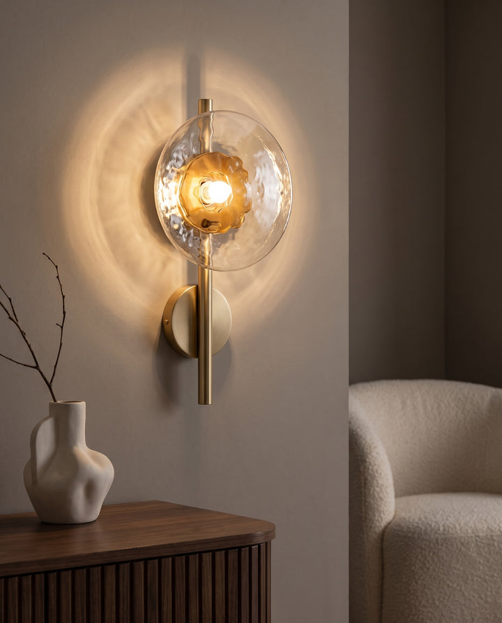 Orbe single head wall sconce in gold with amber glass glowing above a fluted walnut sideboard