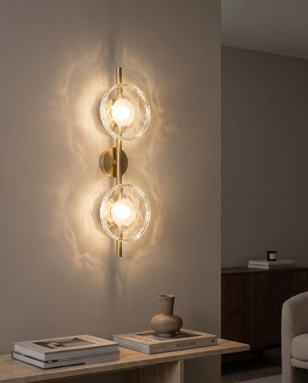 Orbe double head wall sconce in gold with clear glass glowing above a travertine console
