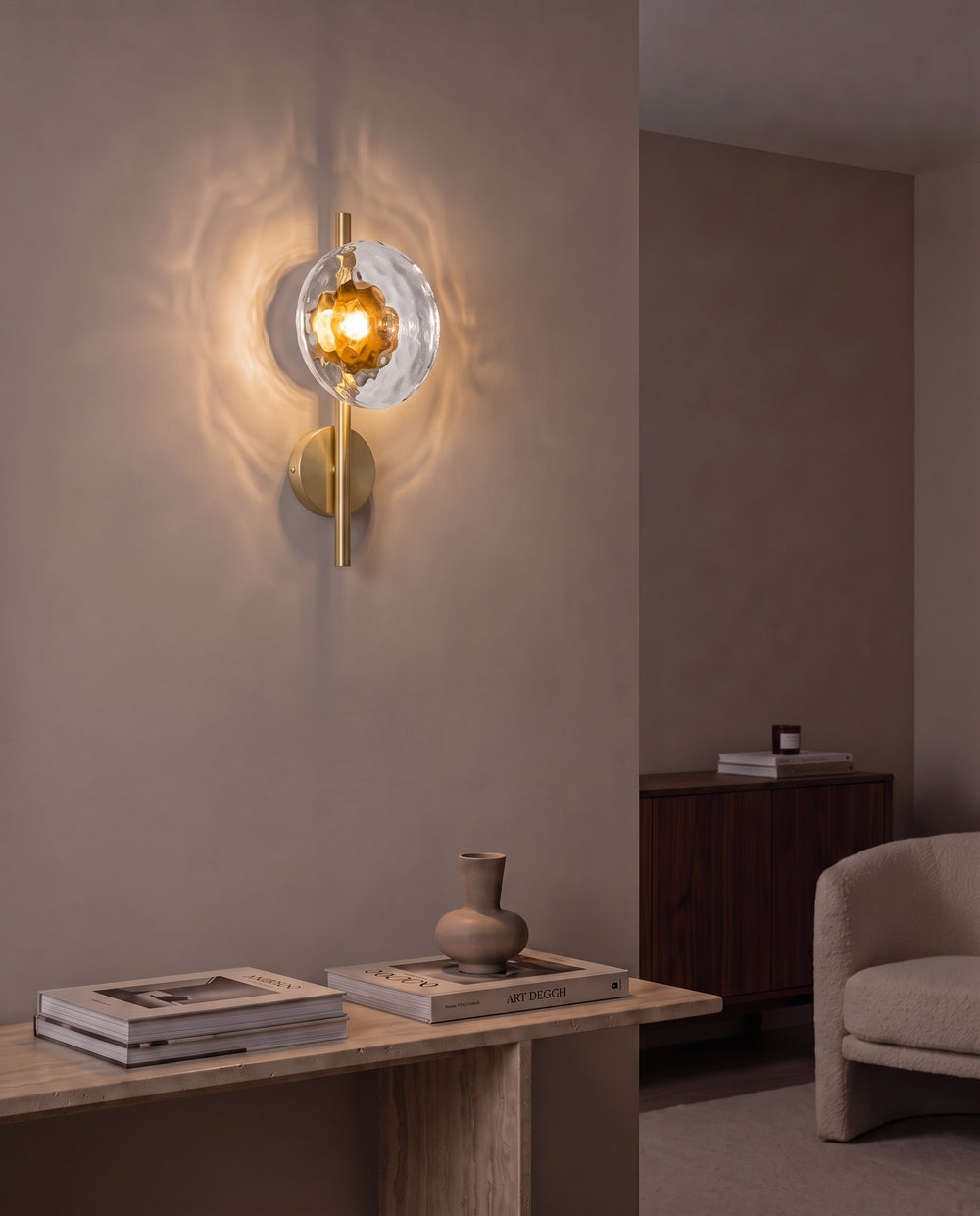 Orbe single head wall sconce in gold with amber glass glowing above a travertine console