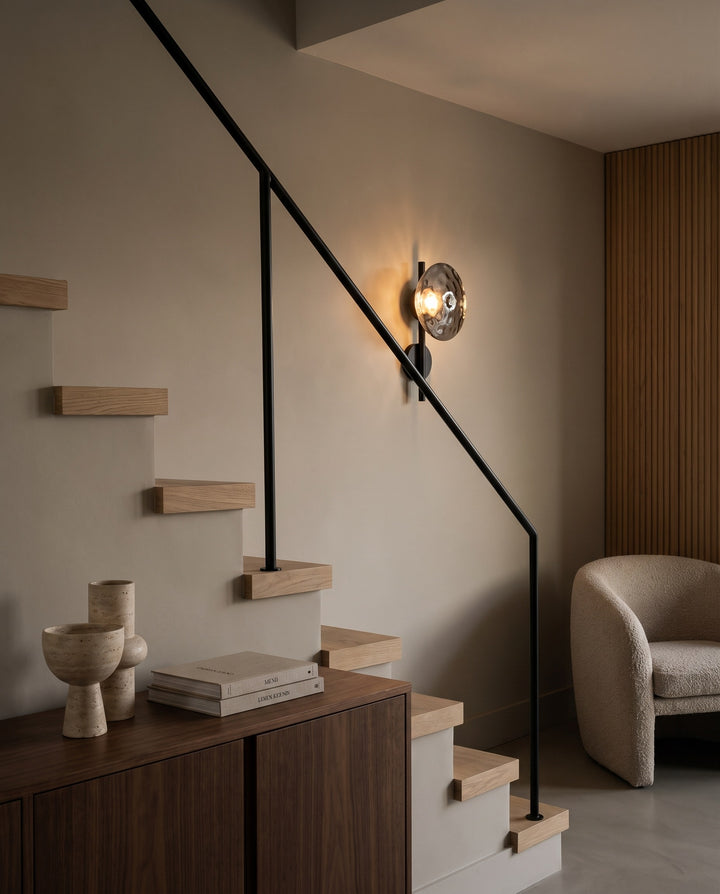 Orbe single head wall sconce in black with smoked glass beside a floating staircase