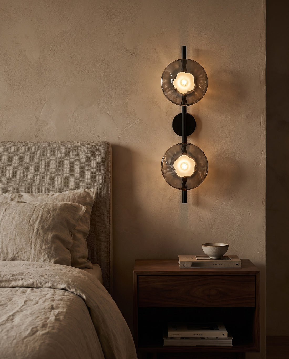 Double head black glass wall sconce with gray glass beside a bed