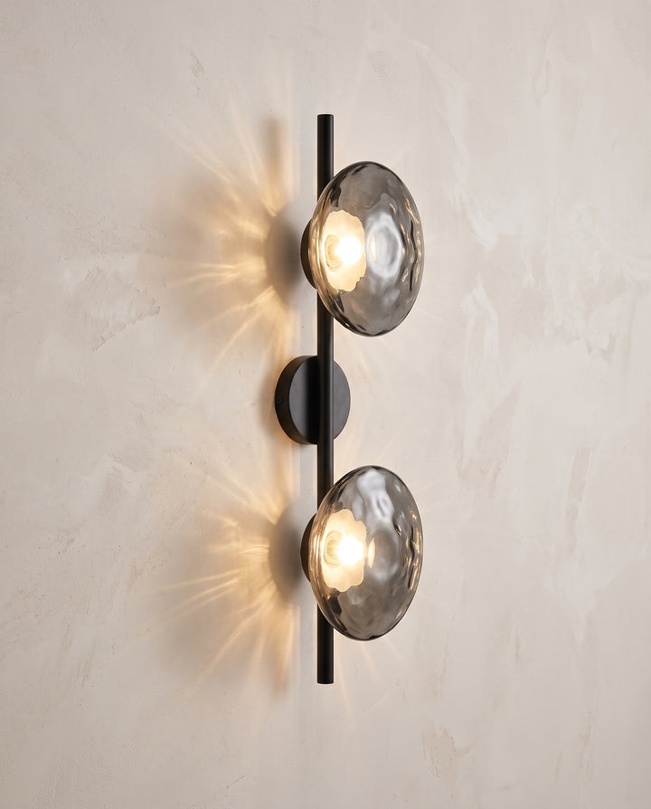 Orbe wall sconce, double head, black with smoked gray glass, lit on a plaster wall