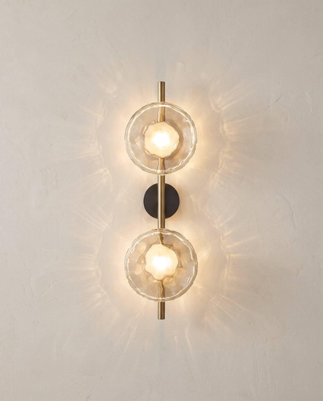 Orbe wall sconce, double head, gold with clear glass, lit on a plaster wall
