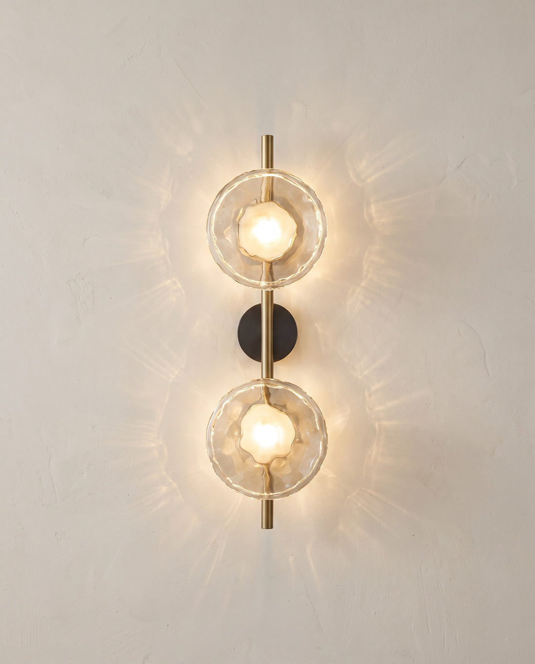 Double head gold glass wall sconce with clear glass lit on a plaster wall