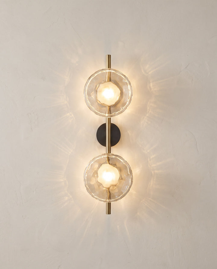 Orbe wall sconce, double head, gold with clear glass, lit on a plaster wall