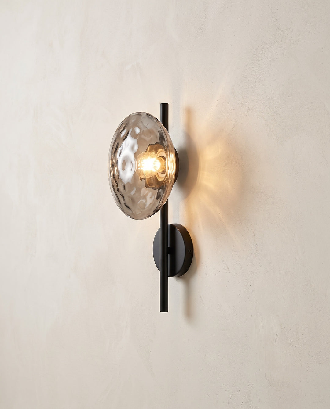 Orbe wall sconce, single head, black with gray glass, lit on a plaster wall