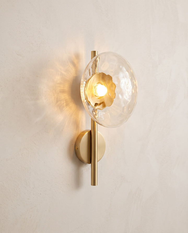 Orbe wall sconce, single head, gold with amber glass, lit on a plaster wall