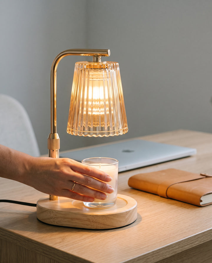 Hand placing a jar candle under the lit shade of the candle warmer lamp on a desk