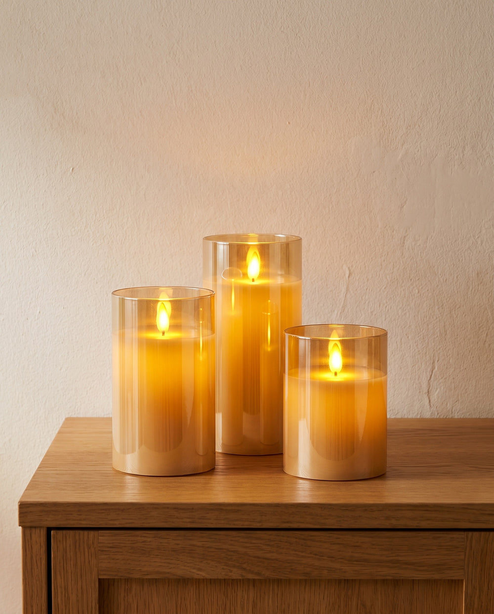 Set of three LED pillar candles in amber glass on an oak sideboard