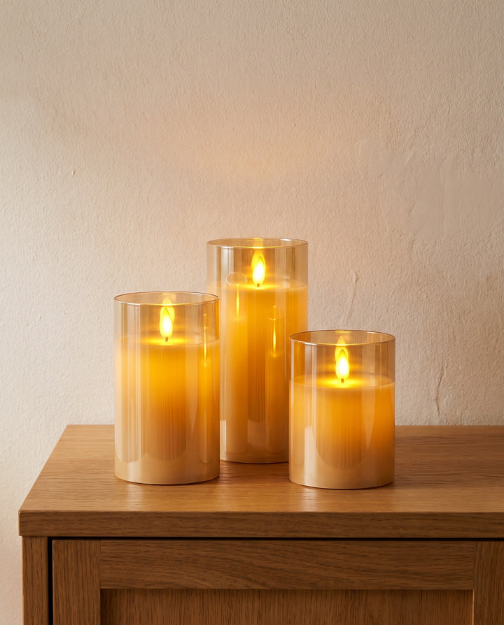 Set of three LED pillar candles in amber glass on an oak sideboard