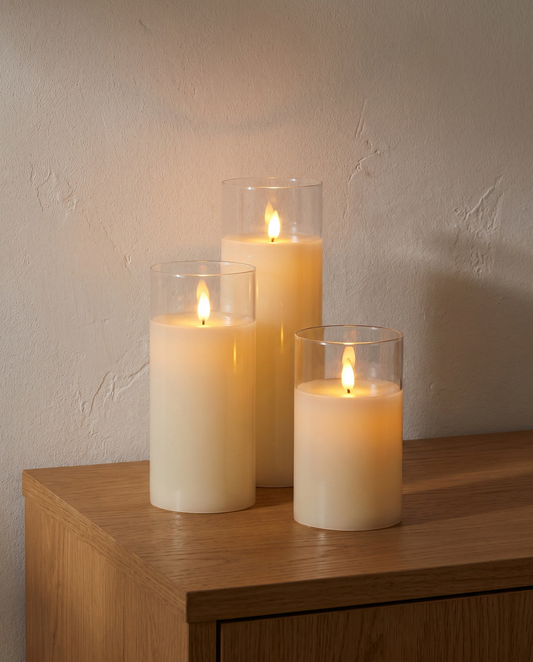 Set of three LED pillar candles in clear glass on an oak sideboard