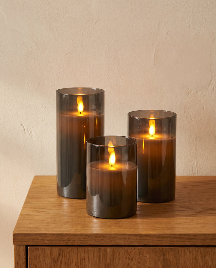 Set of three LED pillar candles in smoked gray glass on an oak sideboard