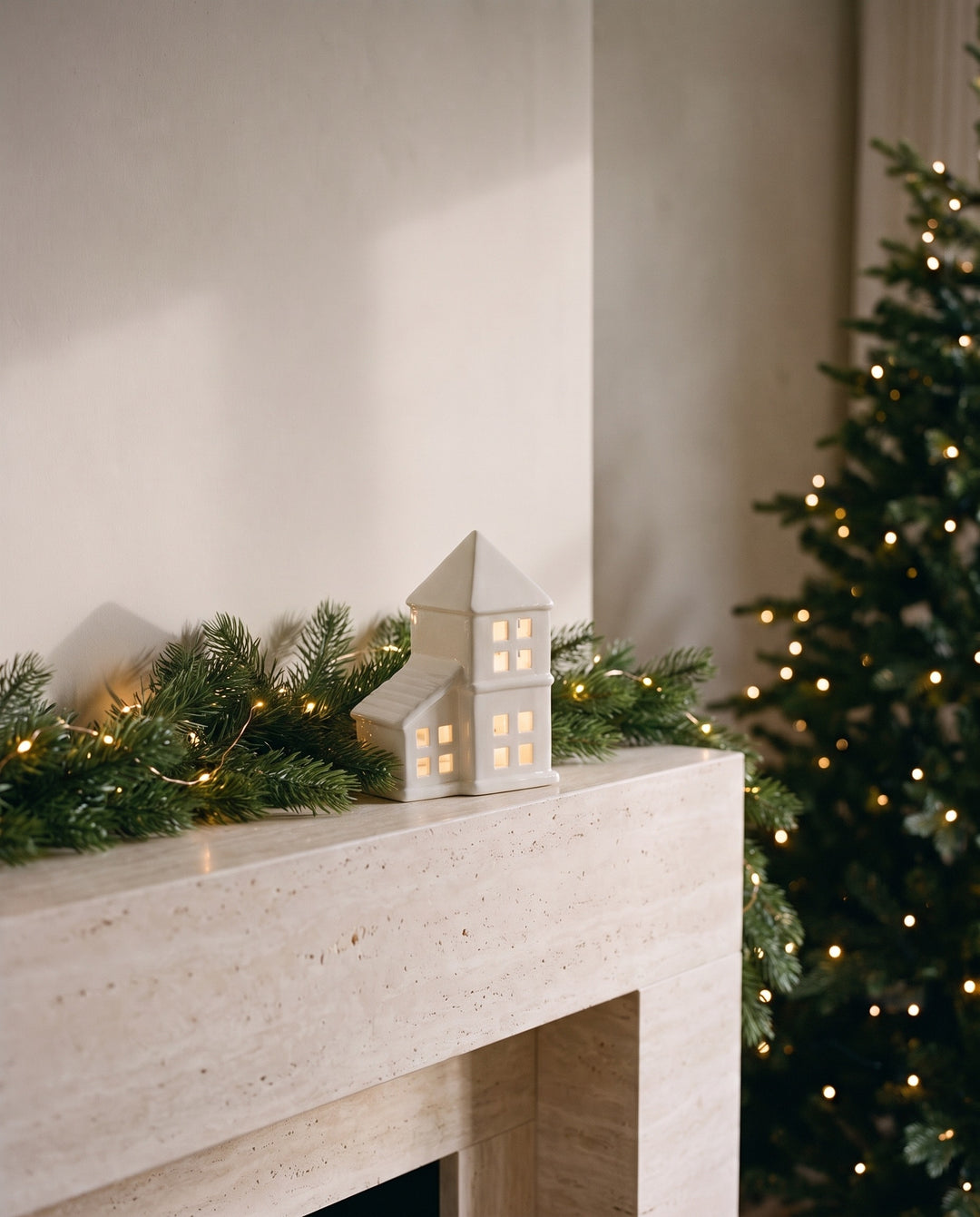 White ceramic house with a pointed pyramid roof and glowing windows on a mantelpiece