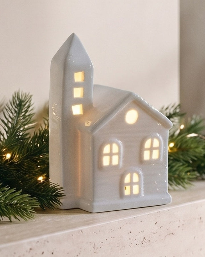 Close-up of the white ceramic house with a bell tower, its windows glowing warm