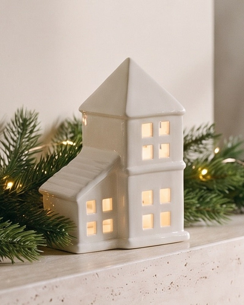 Close-up of the white ceramic house with a pointed pyramid roof, its windows glowing warm