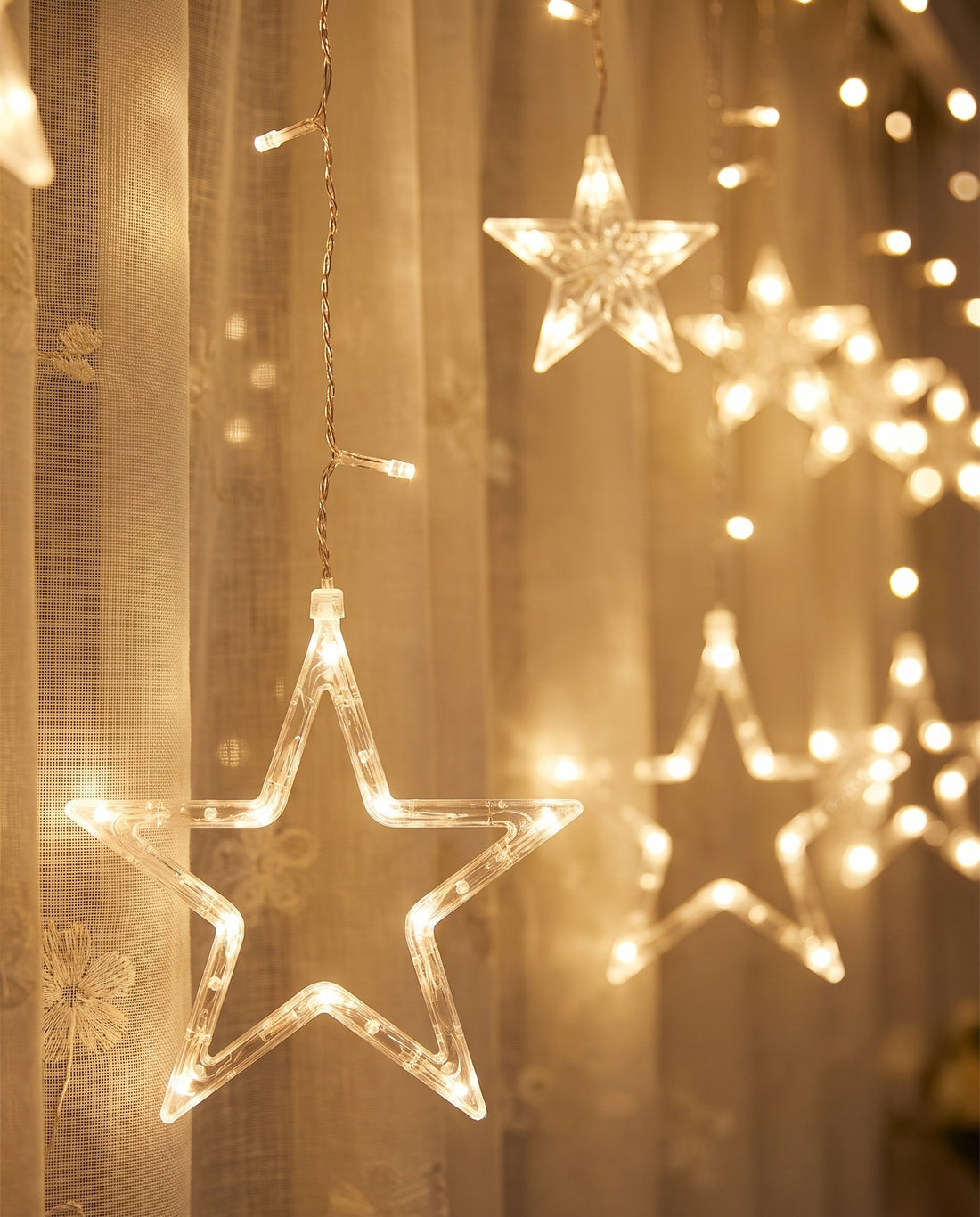 Close-up of warm white LED stars in front of sheer linen curtains