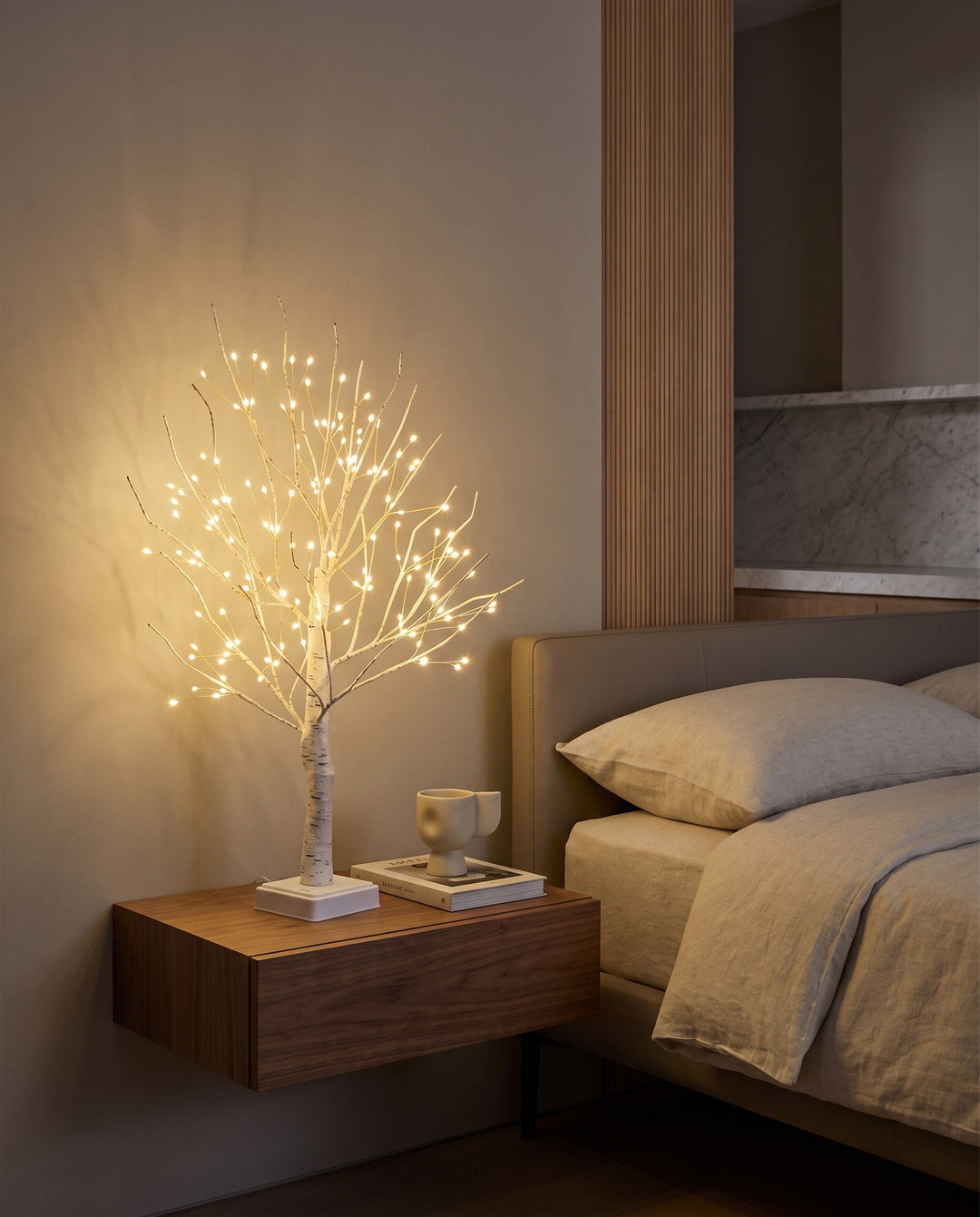Birch tree lamp glowing on a floating bedside table in a modern bedroom