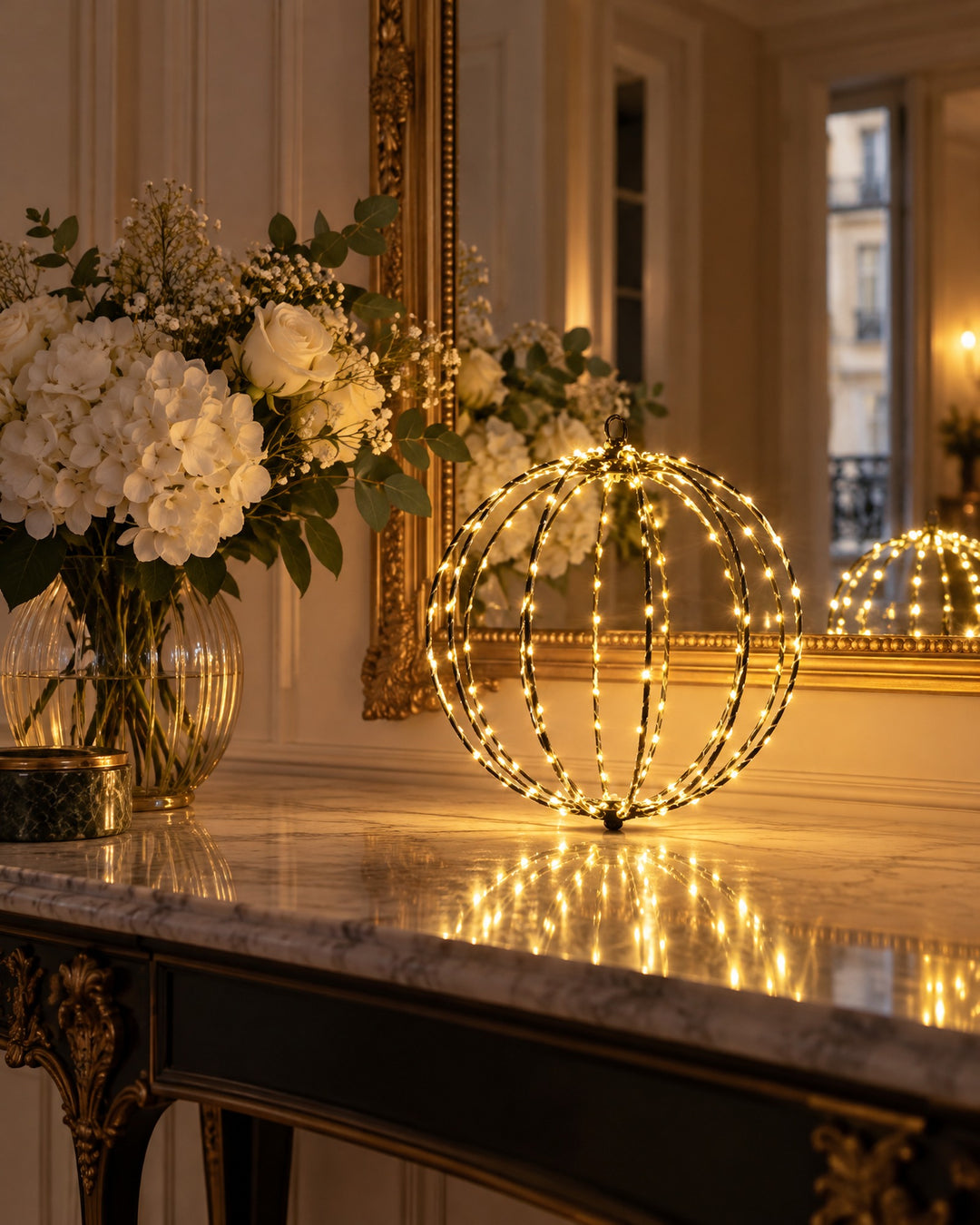 LED globe light glowing on a marble console in front of a gold mirror and white flowers