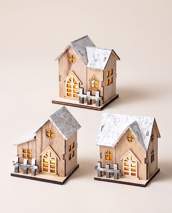 Three wooden LED houses with snowy roofs and glowing windows