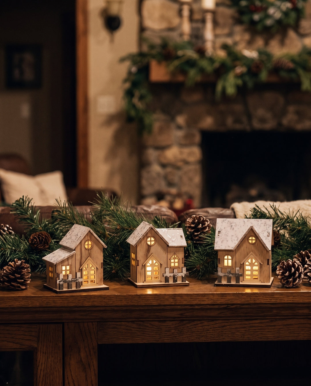 Glowing wooden Christmas houses on a mantel with pine garland