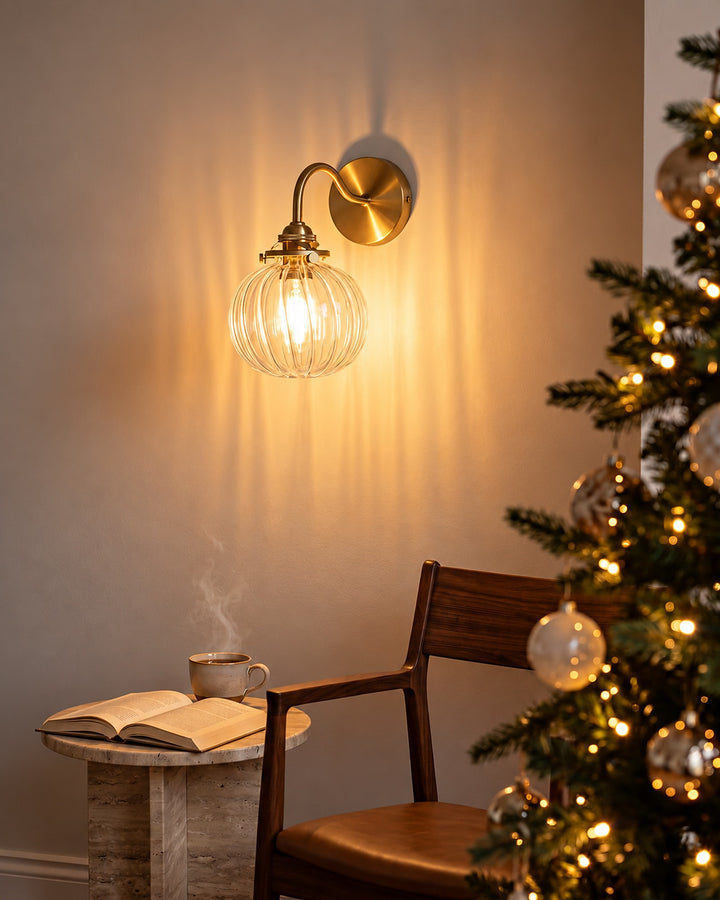 Ribbed glass globe wall sconce lit above a reading chair next to a Christmas tree