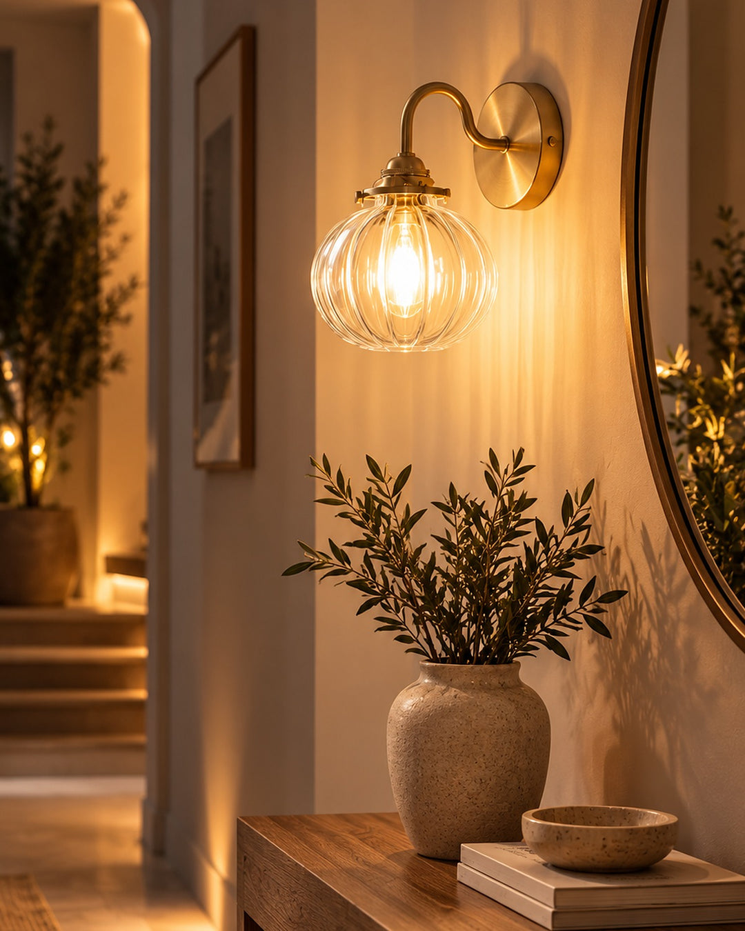 Ribbed glass globe wall sconce lighting an entryway console beside an arched mirror