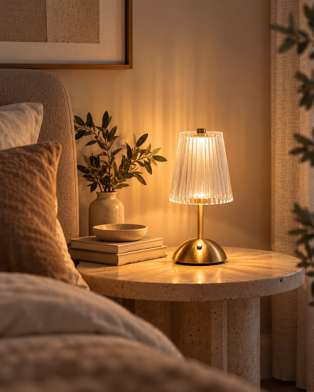 Cordless gold-tone table lamp with a clear ribbed shade glowing on a bedside table
