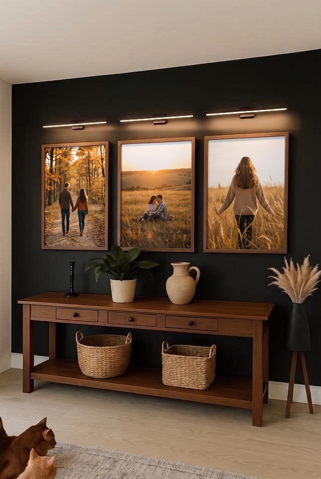 Three LED picture lights above framed family photos on a dark wall over a wooden console